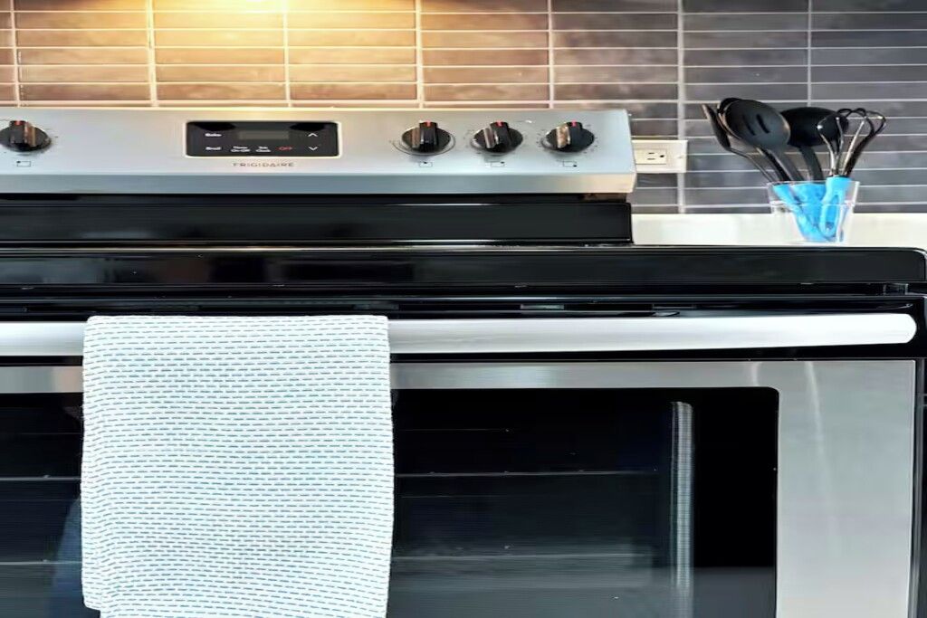 A kitchen with a stainless steel stove, a white towel hanging on the oven door, and a glass container with utensils.