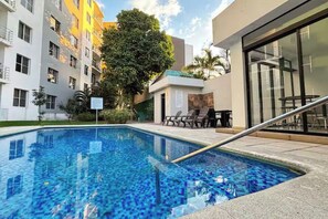 Una piscina con borde de azulejos, rodeada por una terraza con sillas y una mesa.