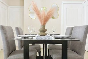 A dining table with a vase of dried flowers, two wine glasses, and a placemat.