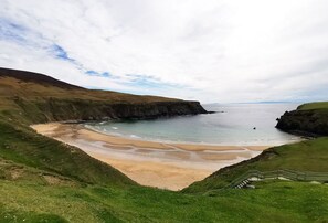 A coastal landscape with a sandy beach, grassy hills, and a staircase leading down to the beach. - Teach Condy's Cottage nestled at the bottom of Sliabh Liag Cliffs, Co. Donegal (Teelin)