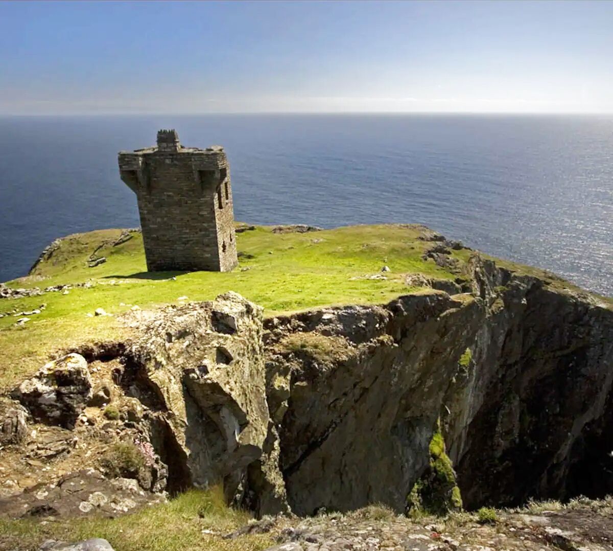 A stone tower on a grassy cliff overlooking the sea.