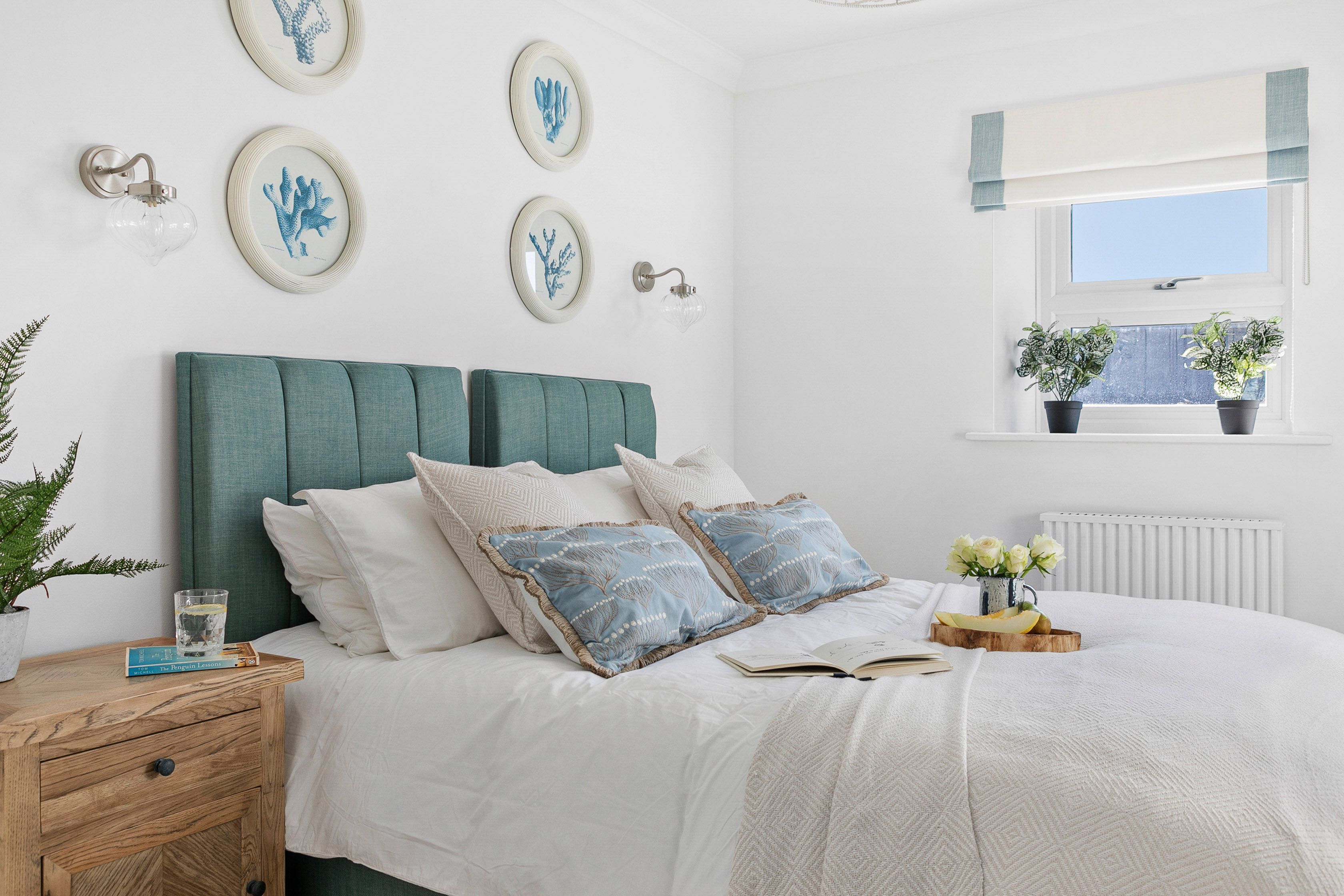 A neatly arranged bedroom with a bed, bedside tables, and a window with potted plants.