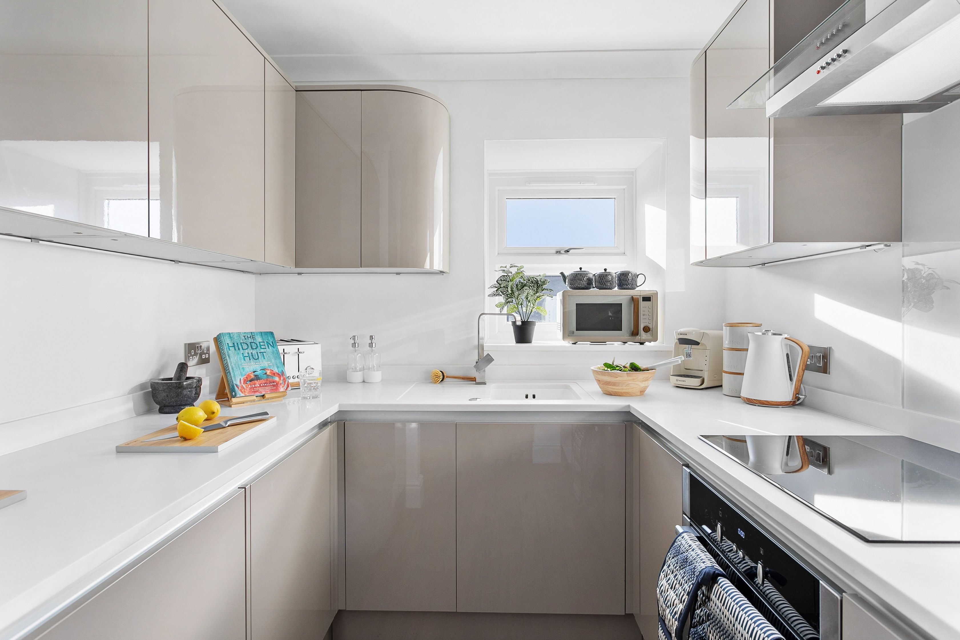 Una cocina moderna con encimera blanca, electrodomésticos de acero inoxidable y una ventana sobre el fregadero.