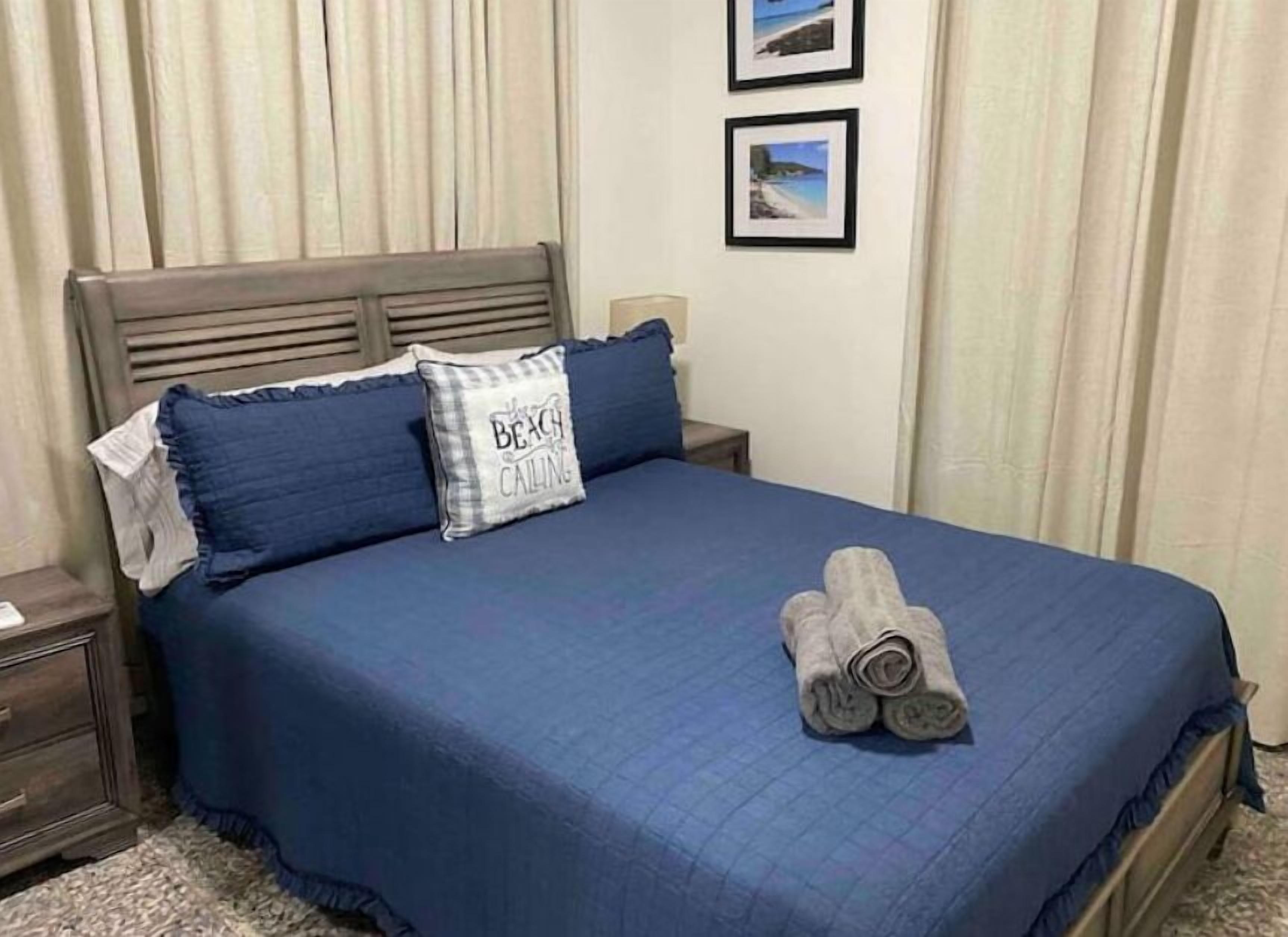 A neatly made bed with a blue bedspread, two pillows, and a folded towel on the bed.