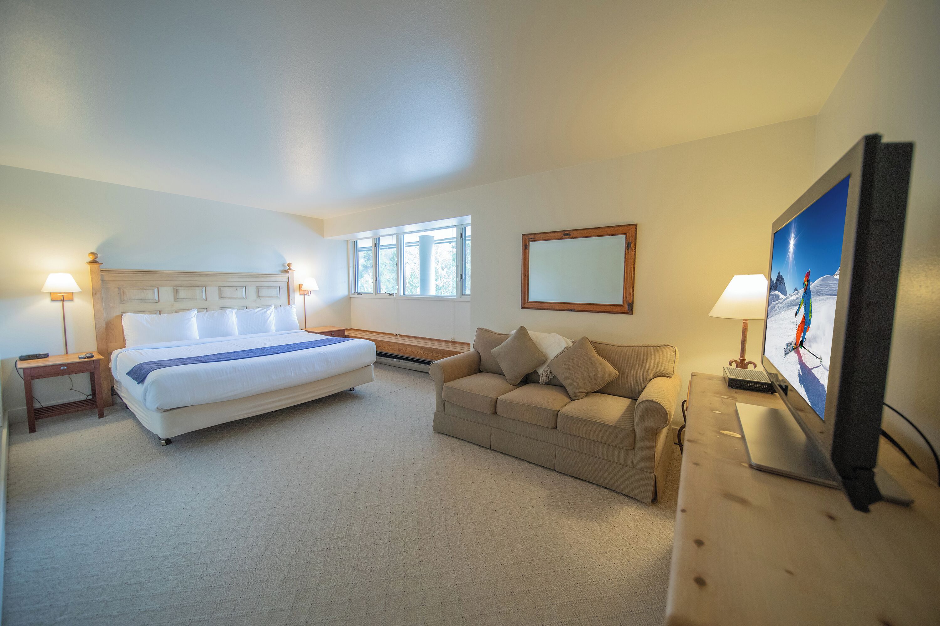 Habitación de hotel con cama, sofá, escritorio y computadora, y televisión.