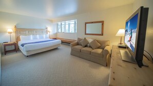 A hotel room with a bed, a sofa, a desk with a computer, and a TV. - Saints John 2515 (Keystone)