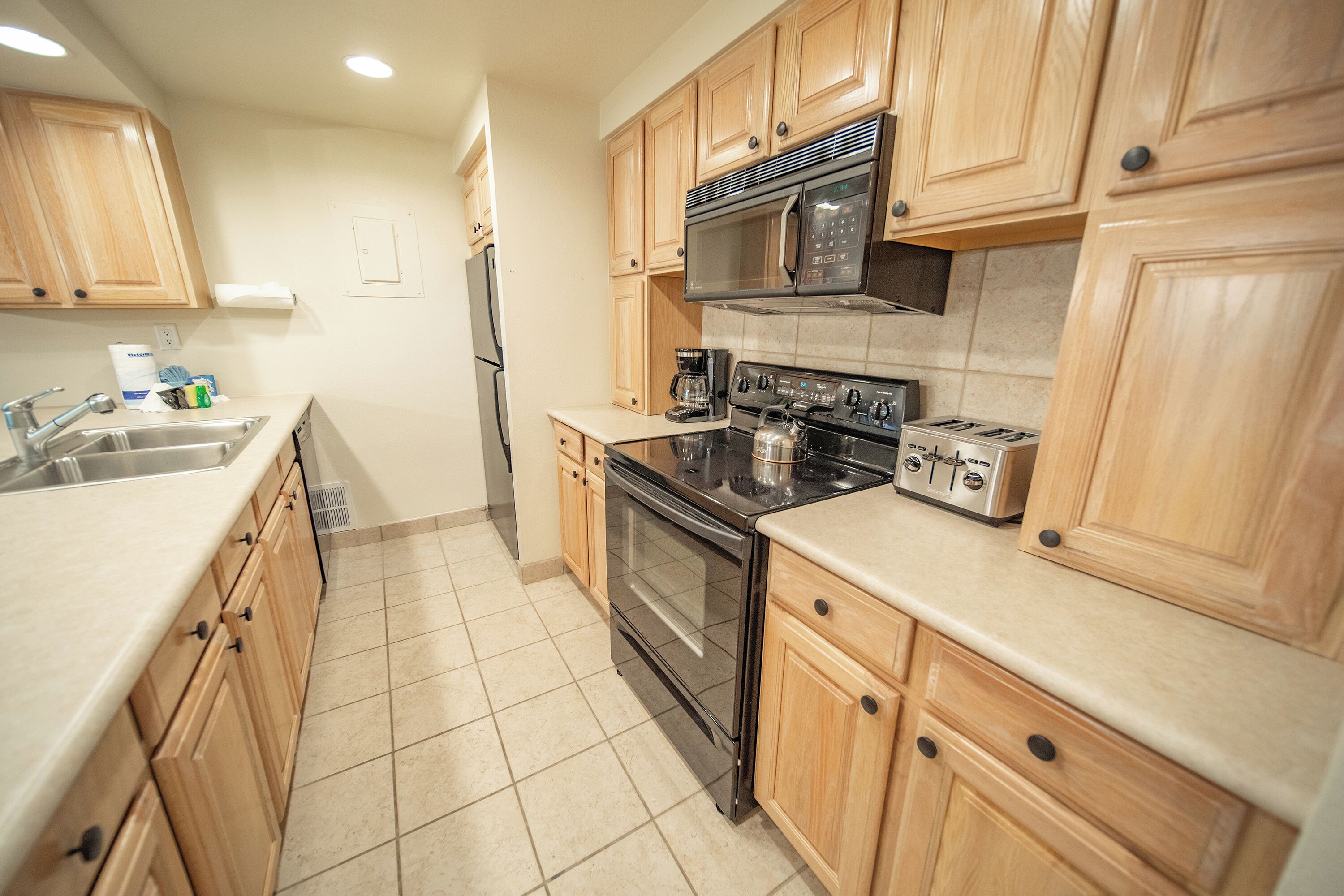 A kitchen with wooden cabinets, a stainless steel sink, a microwave, a stove, and a toaster.