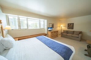Relax in this serene bedroom featuring a large bed, dresser, sofa, and TV.
