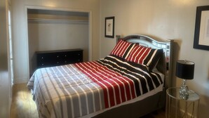 Un dormitorio con cama, ventilador de techo, mesita de noche con lámpara y un cuadro enmarcado en la pared.