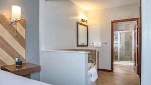 Un baño moderno con ducha, un tocador con espejo y una mesita de noche con un reloj.