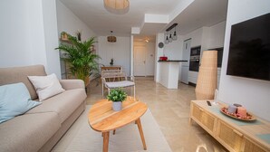 A modern living room with a sofa, coffee table, and a dining area with chairs and a table. - Marina Real apartment 504 (Manilva)