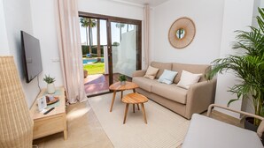 A modern living room with a sofa, a coffee table, a TV, and a view of a pool and greenery outside. - Marina Real apartment 504 (Manilva)