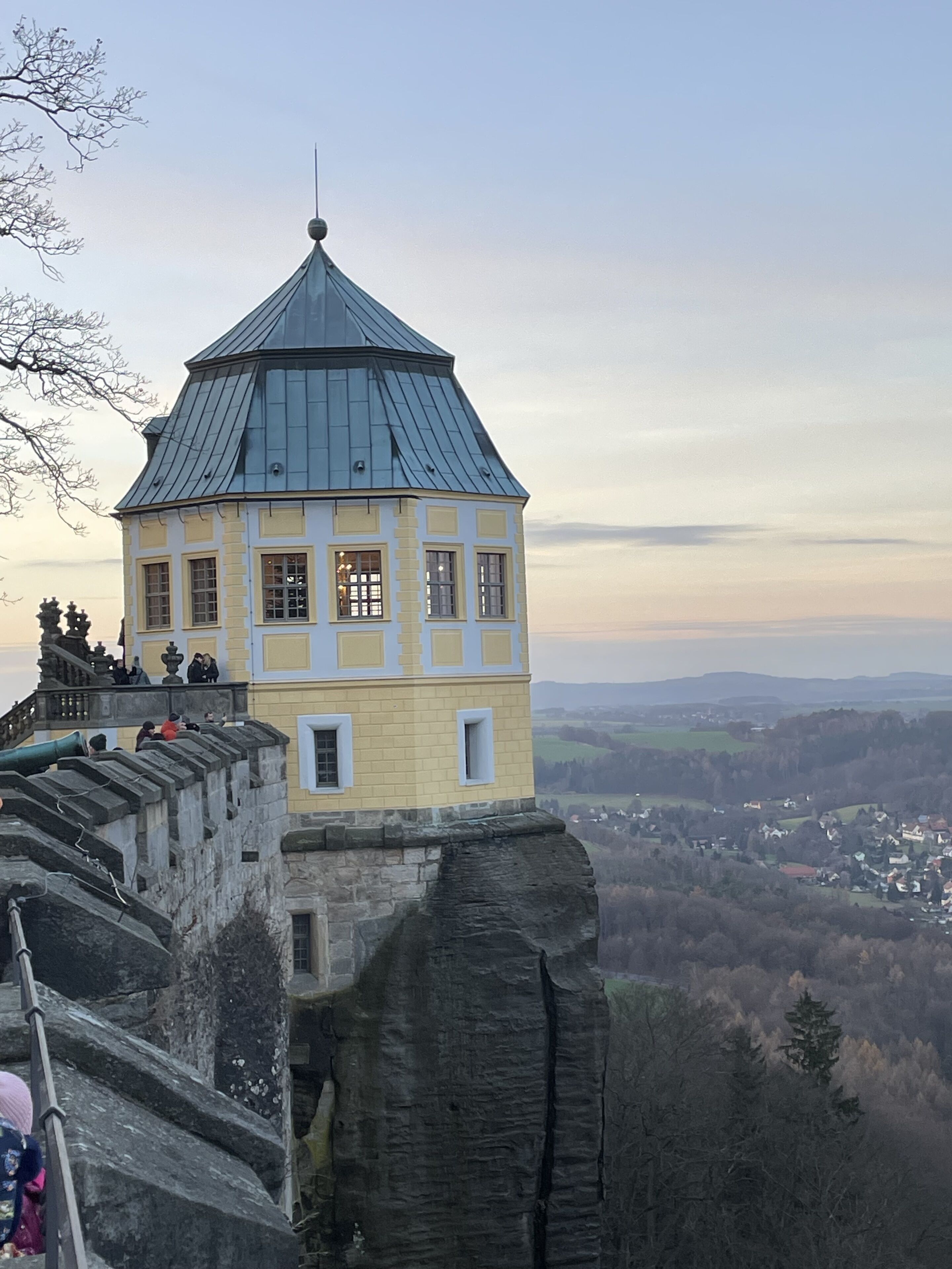 Una torre histórica con techo cónico, ubicada sobre un acantilado rocoso con vistas a un valle.