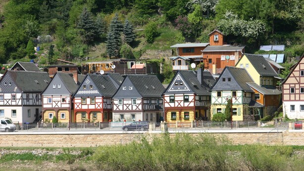 A row of traditional half-timbered houses by a river, with a stone bridge in the foreground.