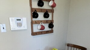 Un coin repas comprenant une table en bois, deux chaises, un panier de fruits et un porte-tasses fixé au mur.