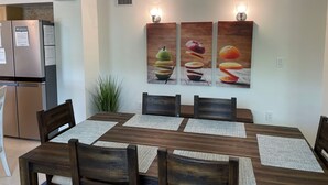 Un comedor con una mesa y sillas de madera, un refrigerador y una lámpara fijada a la pared.