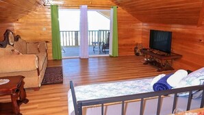 Una cabaña acogedora con interior de madera, una cama, un televisor y un balcón con cortinas.