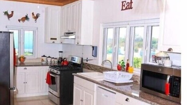 Una cocina moderna con armarios blancos, encimera de granito, estufa, microondas y ventilador de techo.
