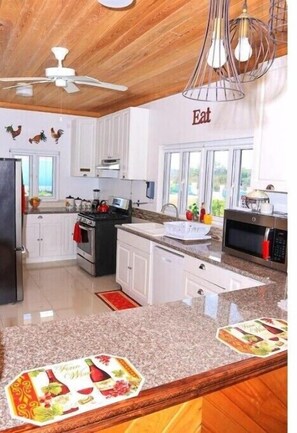 A modern kitchen with white cabinets, a granite countertop, a stove, a microwave, and a ceiling fan. - Redknot Manor Guest house/Hotel
 (Matthew Town)