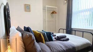 Um quarto com cama, travesseiros, mesa de cabeceira, luminária, janela e armário.