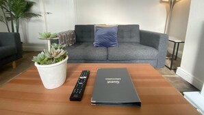 Uma sala de estar com um sofá cinza, uma mesa de centro, um controle remoto Sony e um guia de informações para hóspedes.