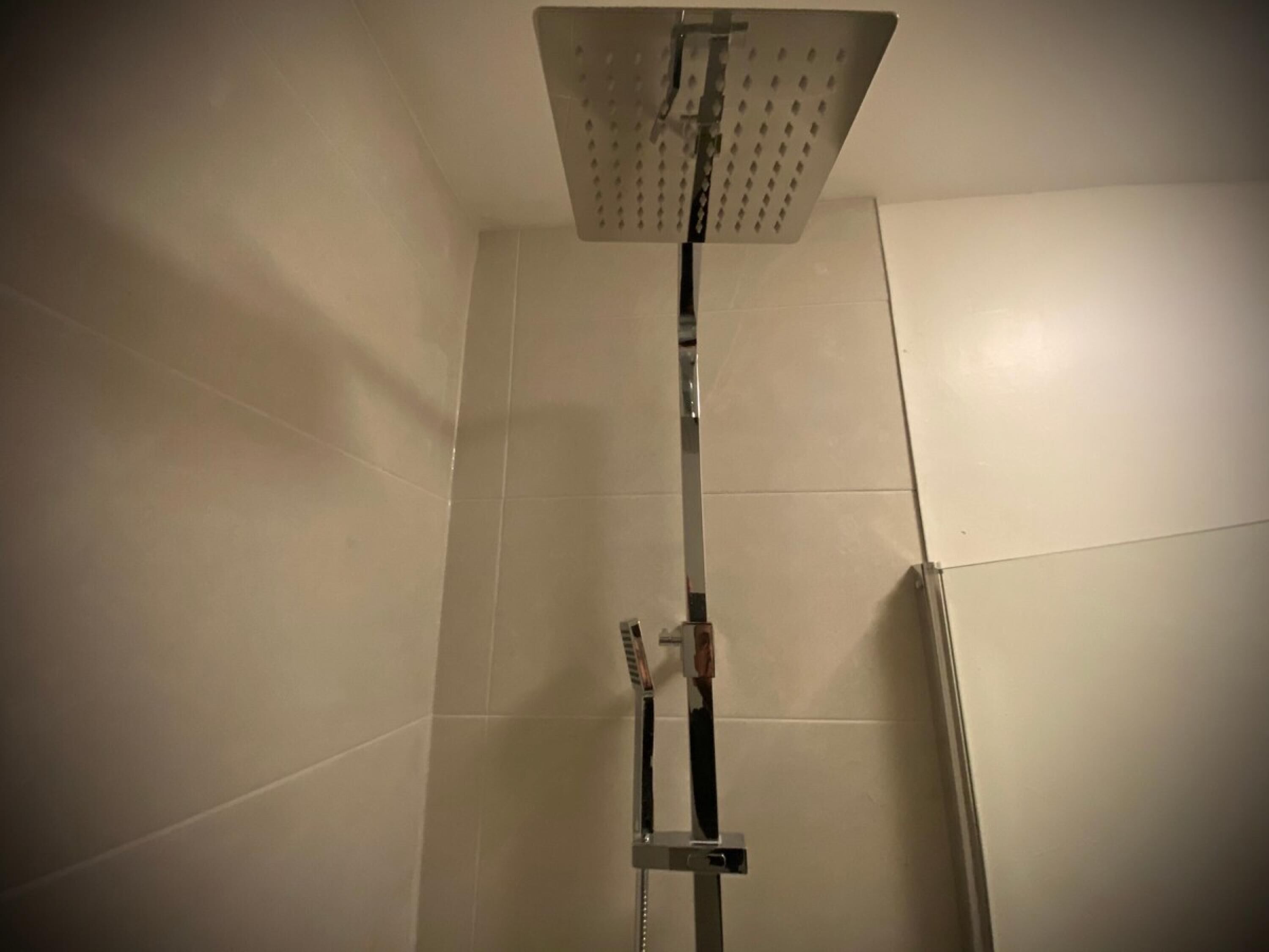 A shower with a square overhead rainhead, a handheld showerhead, and a vertical bar.