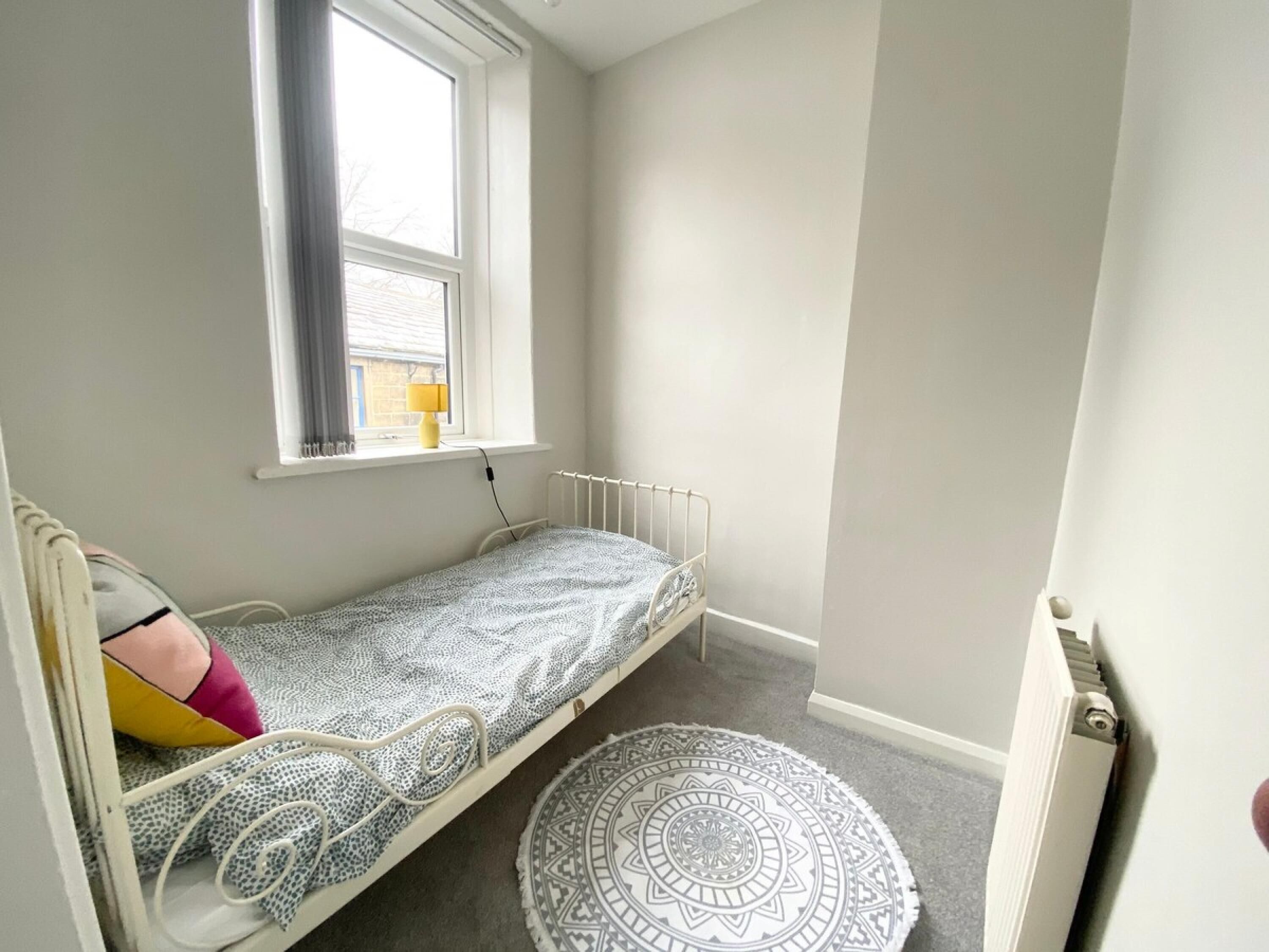 A small, single-bed room with a window, a radiator, and a patterned rug.