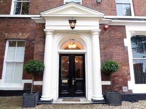 A building with a black door, white columns, and two potted plants. - Claremont The Broderick (Leeds)
