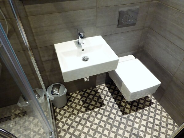 A bathroom with a white sink, a toilet, and a trash bin. The floor has a geometric tile pattern. - Claremont The Broderick (Leeds)