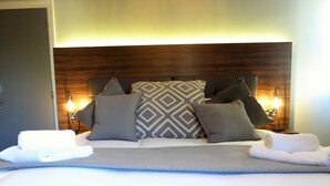 A neatly made bed with a patterned pillow, a rolled towel, and a bedside lamp. - Claremont The Corson (Leeds)