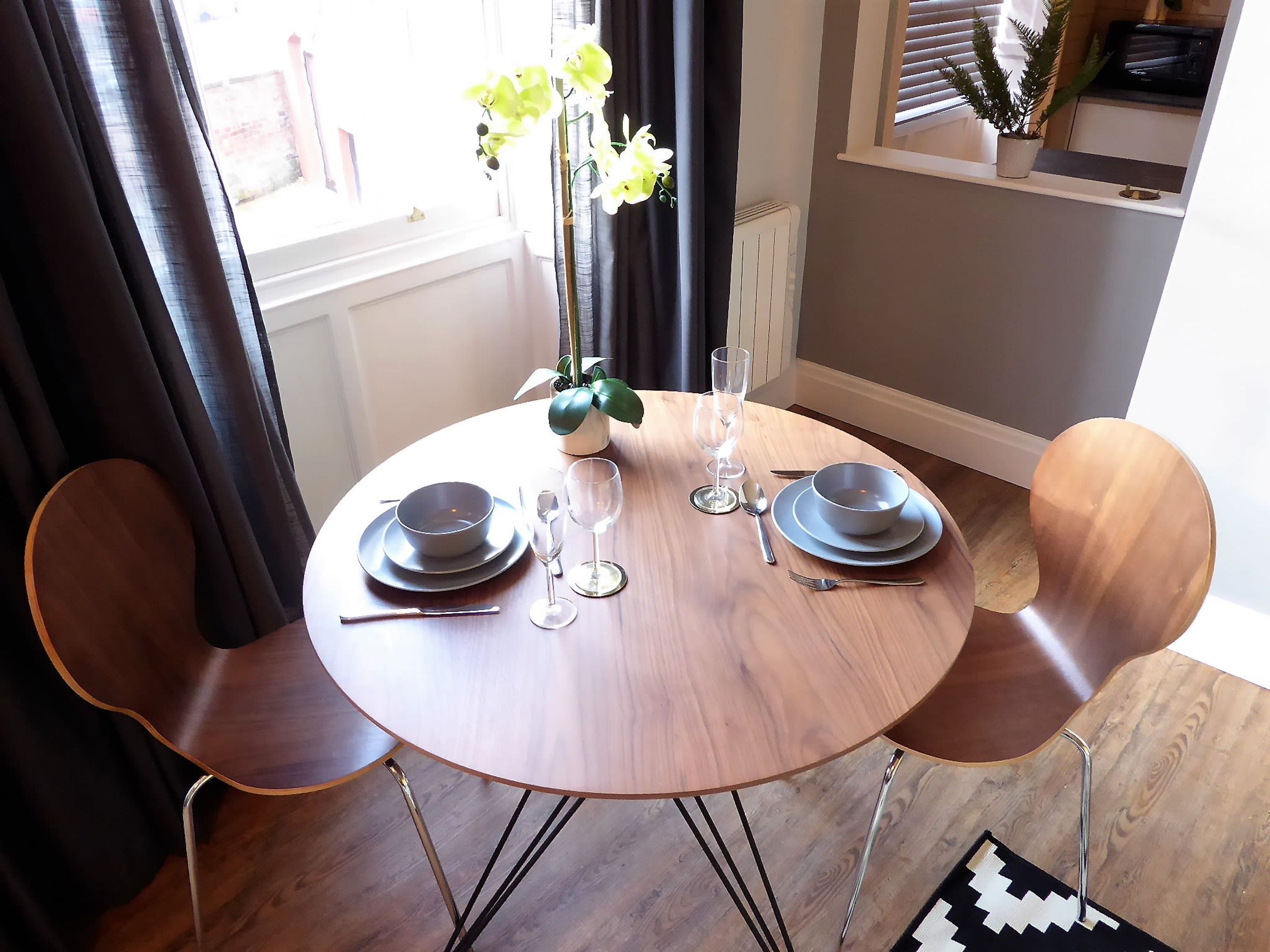 Une table à manger avec deux chaises, un vase rempli de fleurs et un ensemble de bols pour deux personnes.