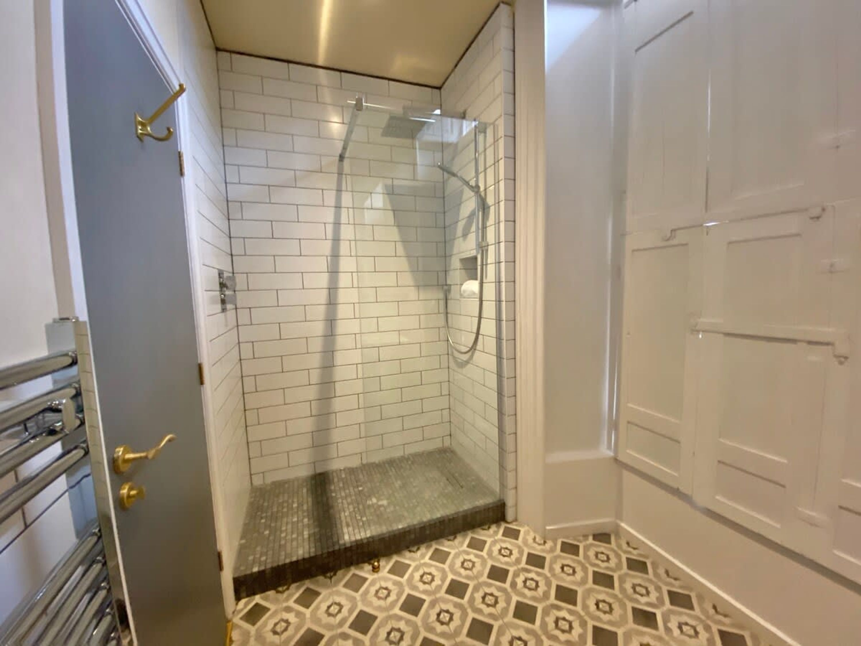 A bathroom with white tiled walls, a shower area, and patterned floor tiles.