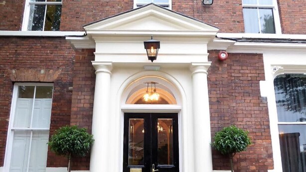 Un edificio con puerta negra, columnas blancas y dos plantas en macetas.