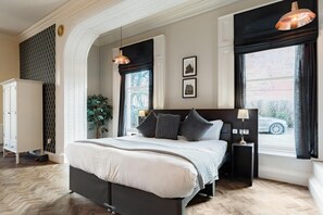 A bedroom with a large bed, two bedside tables, a wardrobe, and a window with a view of a car.