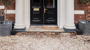 Une porte noire à deux vantaux, surmontée d’un fronton blanc et flanquée de colonnes, intégrée à un bâtiment en briques.