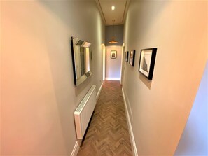 Stylish hallway with a large mirror, framed artwork, and a radiator leading to a cozy room.