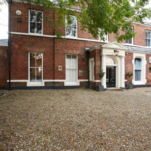 A brick building with a gravel driveway and a small entrance with a door and columns. - Claremont The Matcham (Leeds)