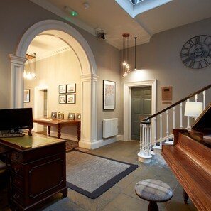 A spacious room with a grand piano, a desk with a computer, and a comfortable seating area. - Claremont The Matcham (Leeds)