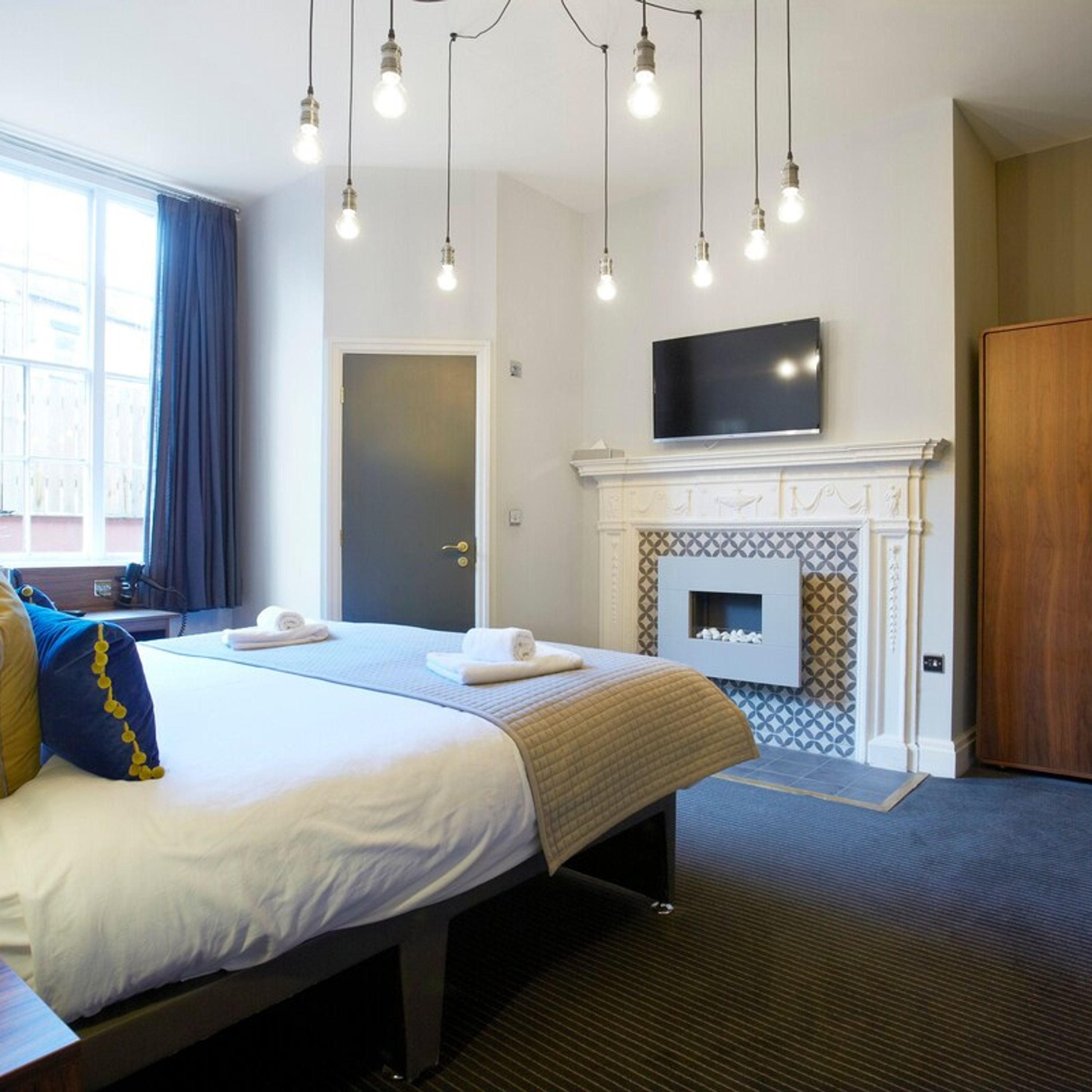 Habitación de hotel con cama, televisión de pantalla plana, chimenea y ventana con cortinas.