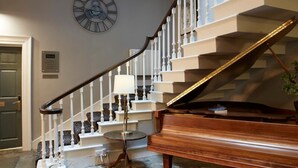 A grand piano in a spacious living area with a staircase leading to an upper floor. - Claremont The Matcham (Leeds)