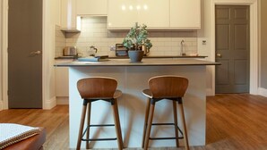 A modern kitchen with white cabinets, a central island with two bar stools, and a pendant light above. - Claremont The Matcham (Leeds)