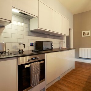 A modern kitchen with white cabinets, a stainless steel oven, a microwave, and a kettle. - Claremont The Matcham (Leeds)