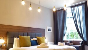 A hotel room with a large bed, a wooden headboard, and a window with dark curtains. - Claremont The Matcham (Leeds)
