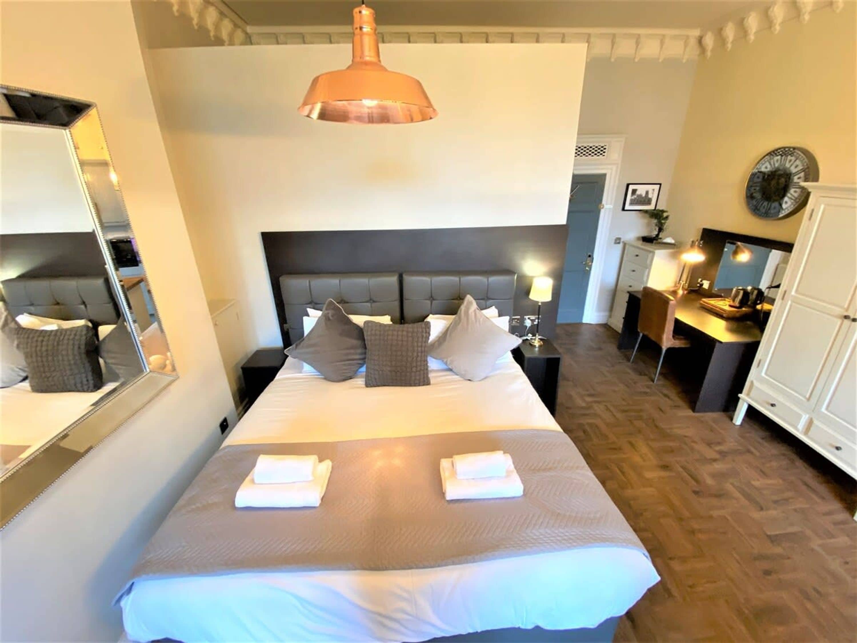 A hotel room with a large bed, bedside tables, a desk, a mirror, and a hanging pendant light.