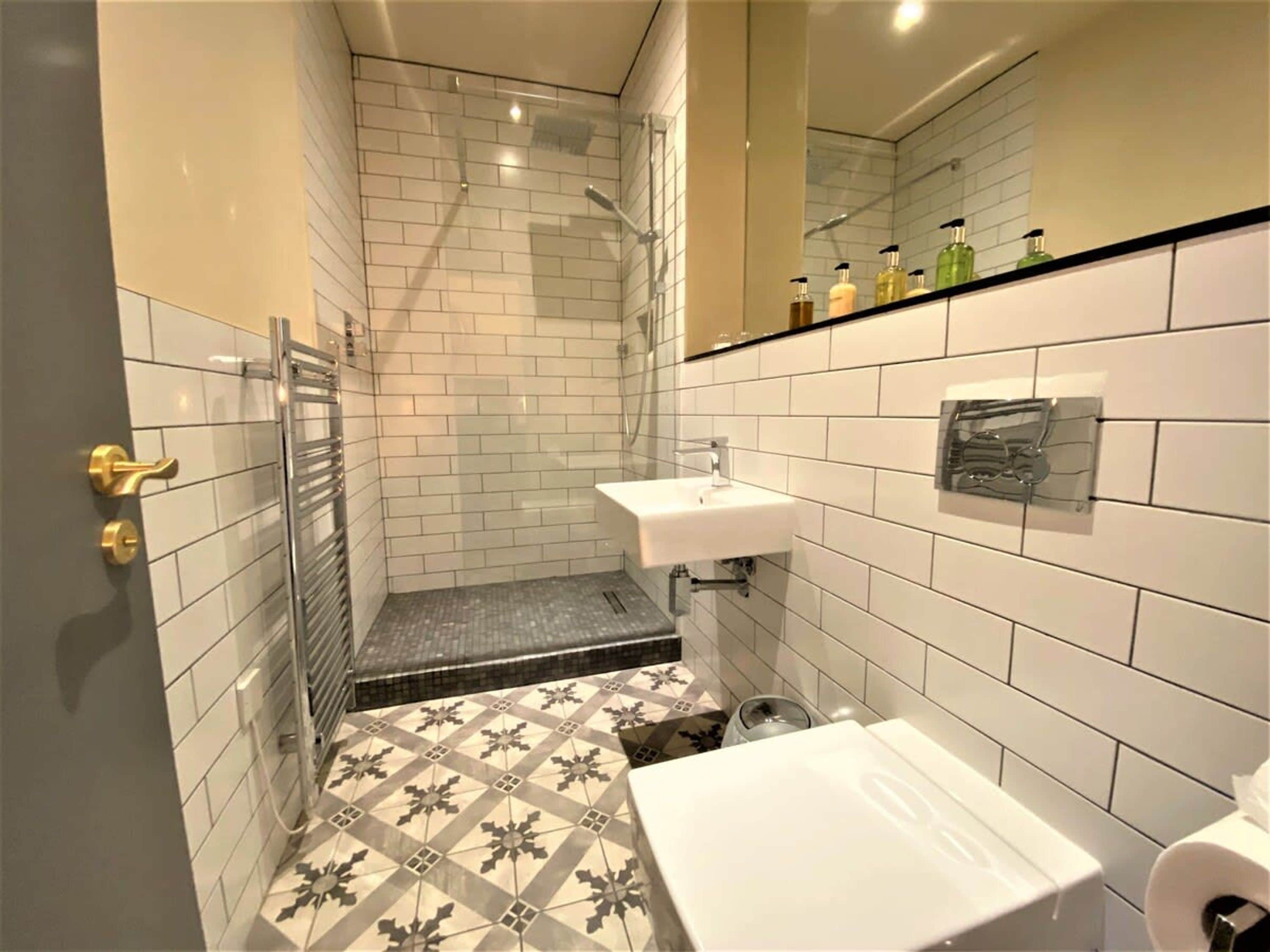 A bathroom with white tiled walls, a shower, a sink, and a toilet.