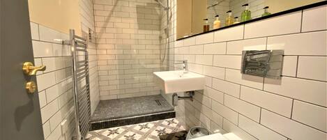 A bathroom with white tiled walls, a shower, a sink, and a toilet.