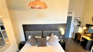 Une chambre d’hôtel avec un grand lit, une tête de lit, des tables de chevet, un bureau et un miroir.