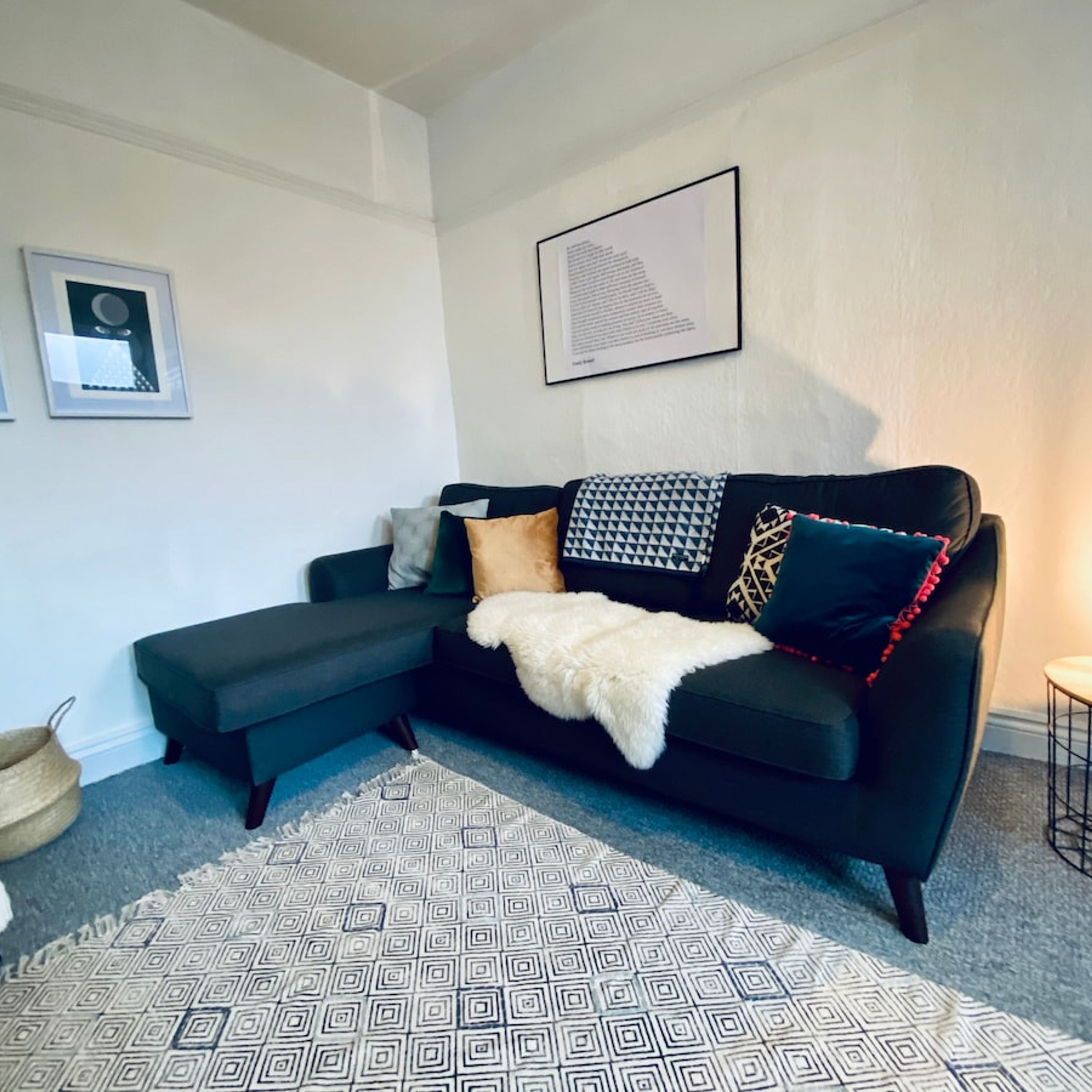 A modern living room with a black sectional sofa, a patterned rug, and a framed abstract artwork on the wall.