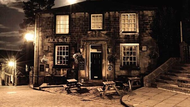 A stone building with a sign reading "BLACK BULL" at night.