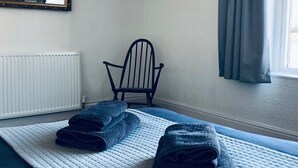 A room with a bed, a chair, a radiator, and a window with curtains.